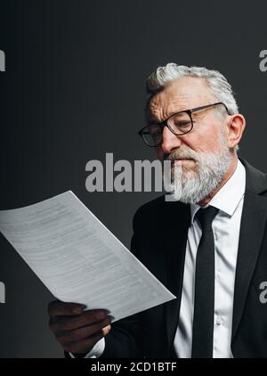 Reifer bärtiger Geschäftsmann trägt eine Brille in schwarzem Anzug mit Lesehalter Dokument in der Hand isoliert auf schwarz Stockfoto