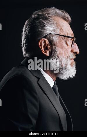 Portrait von stattlichen älteren CEO posiert im Profil, in schwarzen Anzug auf dunklem Hintergrund gekleidet Stockfoto