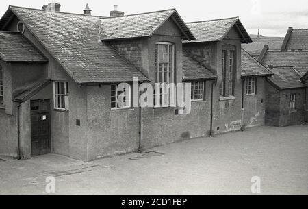 1950er Jahre, historisches Bild aus dieser Zeit zeigt einen Teil der viktorianischen Dorf Grundschule und Spielplatz, Llandyssil, Powys, Wales. Das 1866 erbaute Gebäude wurde von Thomas Henry Wyatt entworfen, einem anglo-irischen Architekten, der 1870 zum Präsidenten des Royal Institute of Briitsh Architects gewählt wurde und 1873 die Royal Gold Medal for Architecture erhielt. Die Schule wurde 1950 geschlossen und Teile davon wurden erst 2010 durch eine Spendenaktion gerettet, um die Schulhalle zu einem lokalen Gemeindezentrum zu machen. Stockfoto