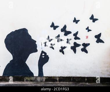 Kunstwerk an einer Wand, Mann bläst Schmetterlinge im Gegensatz zu Blasen In Saltburn by the Sea, North Yorkshire, England, Großbritannien Stockfoto