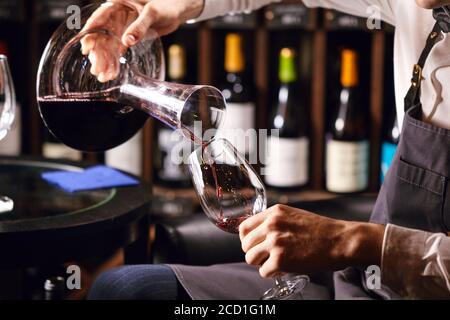 Geübter Sommelier gießt Wein aus dem Dekanter in das Weinglas. Degustation des Weinprozesses in der Weinboutique, Nahaufnahme. Stockfoto