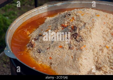 Nationale Nahrung der östlichen Völker. Pilaf in einem großen Kessel. Reis und Lamm über dem Feuer gekocht. Kochen von nationalen Speisen Stockfoto