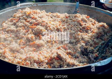 Nationale Nahrung der östlichen Völker. Pilaf in einem großen Kessel. Reis und Lamm über dem Feuer gekocht. Kochen von nationalen Speisen Stockfoto