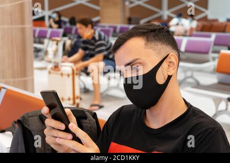 Ein Typ wartet in der Flughafenlounge in einer medizinischen Maske auf einen Flug. Flugreisen während der Coronavirus-Pandemie Stockfoto