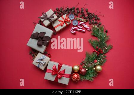 Weihnachtskranz aus Geschenkschachteln, Tannenzweigen, Tannenzapfen, Weihnachtskugeln, Kerzen, Lutscher und Zimt auf rotem Hintergrund oben V Stockfoto