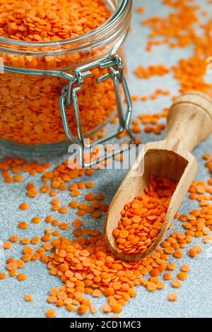 Rote Linsen in einem Glasglas und in einer Holzlöffel auf einem grauen Beton Hintergrund Nahaufnahme. Gesunde Ernährung. Ernährung. Das Konzept von vegetarisch und vegan. Sele Stockfoto