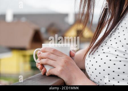 Nahaufnahme Weiberhand mit einer weißen Tasse mit Kaffee Oder Tee auf dem Balkon mit einer tollen Aussicht Die Berge und Villen Dächer Stockfoto