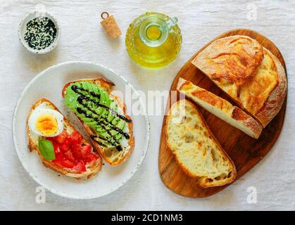 Weizenbrot-Sandwiches mit Frischkäse (Ricotta), Avocado, Eier, Tomaten, Basilikum, schwarzem und weißem Sesam, Balsamico. Leckeres gesundes Frühstück für unterwegs Stockfoto