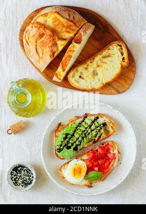 Weizenbrot-Sandwiches mit Frischkäse (Ricotta), Avocado, Eier, Tomaten, Basilikum, schwarzem und weißem Sesam, Balsamico. Leckeres gesundes Frühstück für unterwegs Stockfoto