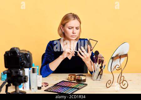 Frontansicht der traurigen jungen Make-up-Künstlerin hält Eyeshades Palette, enttäuscht Ausdruck, doesnt wie neue Produkte, Blick nachdenklich, schießen Stockfoto