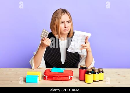 Frontansicht der verwirrt jungen blonden Frau hält Tabletten und liest medizinische Broschüre, Stirnrunzeln Gesicht in Abneigung, nimmt Medizin durch Rezept, fühlt sich verwirrt Stockfoto