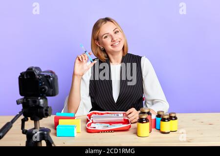 Schöne gut aussehende Ärztin hält Spritze, starrt in der Kamera mit breitem Lächeln, zeigt ihre Zahnspange, erzählt über Impfstoffe, Injektionen und dru Stockfoto