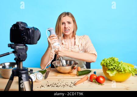 OPPS, etwas geht schief. Isolierte Aufnahme von niedlichen Blogger Mädchen versucht neues Rezept, hält Mixer, schaut in die Kamera mit miserablen Gesichtsausdruck, will Stockfoto