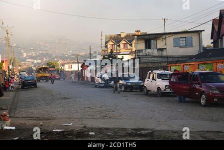 Fianarantsoa, Madagaskar - 06. Mai 2019: Morgenszene in Fianarantsoa - Leute, die die Straße gehen, Kinder gehen zur Schule, Autos, meistens Taxis, die Seite geparkt sind Stockfoto