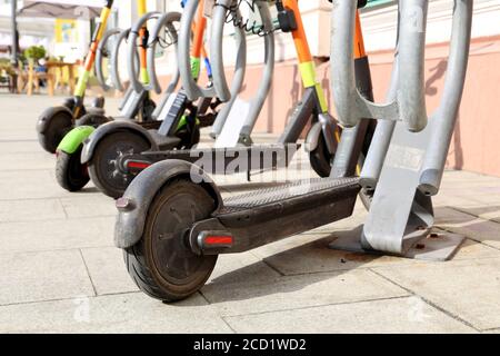 Elektrische Roller hintereinander auf dem Parkplatz. Stadtradverleih, öffentliche E-Roller auf der Straße Stockfoto