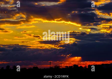 Ein sehr dramatischer Himmel voller Gelb, Blau und Orangen. Kontrastierende Wolken während des Sonnenuntergangs von der untergehenden Sonne beleuchtet. Hell gesättigt natürlich Stockfoto