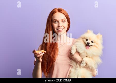 Gut aussehende fröhliche Mädchen mit langen roten Haaren kümmert sich um ihr Haustier. Nahaufnahme Porträt, isoliert blauen Hintergrund, Studio erschossen, Freundschaft und Liebe Stockfoto