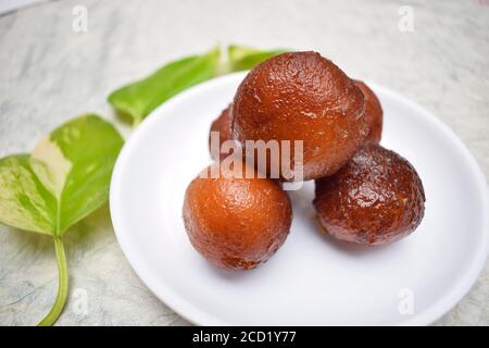 Nahaufnahme von Gulab jamun süßem indischen Dessert auf weißem Hintergrund auf weißem Teller. Dekoriert mit moneyplant Blätter. Stockfoto