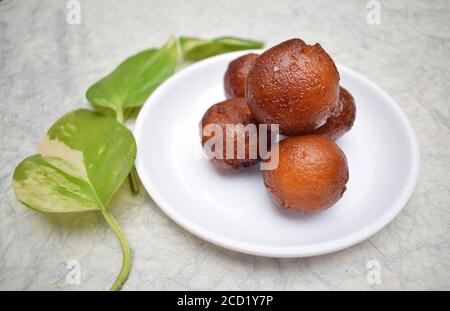 Nahaufnahme von Gulab jamun süßem indischen Dessert auf weißem Hintergrund auf weißem Teller. Dekoriert mit moneyplant Blätter. Stockfoto