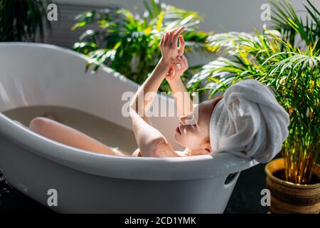 Schöne junge Frau, die ihren Körper im Wasser verwöhnt und mit Mineralölen in der entspannenden Atmosphäre des Hotel-Spa-Bereichs am sonnigen Morgen ein Bad nimmt Stockfoto