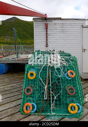 Bunte Krabbennetze, die an der alten Mauer der Fischerfabrik aufgeschichtet sind Mit rotem Kranausleger bereit für den nächsten Einsatz Stockfoto