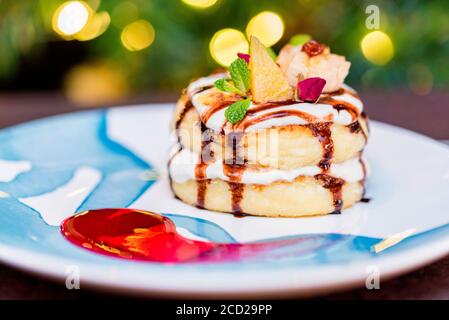 Hüttenkäse Pfannkuchen oder Syrniki mit Sahne, Obstmarmelade und Blumendekoration Stockfoto