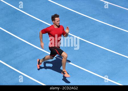 Sprinter Mann läuft auf blauen Spuren Spuren im Leichtathletik-Stadion in High Speed Draufsicht. Männlicher Läufer im intensiven Sprinttraining. Laufen Sie Sport Stockfoto