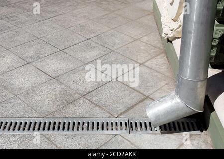 Eine technische Struktur ein Downspout mit einem Drainagerost vor dem Hintergrund eines grauen Stein Granit Gehweg aus quadratischen Fliesen mit Kopieplatz, si Stockfoto