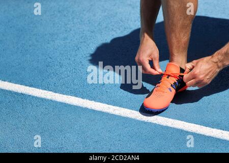 Der Athlet Sprinter bereitet sich auf das Laufen vor und bindet Schnürsenkel auf den Laufstrecken des Stadions. Mann Läufer Vorbereitung für Cardio-Training im Freien. Fitness und Stockfoto