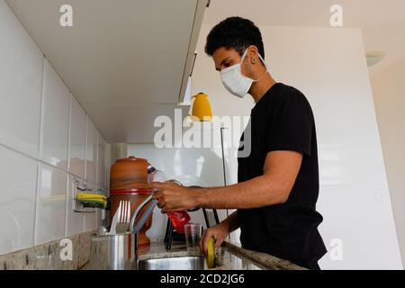 Mann Erwachsene schwarz trägt Coronavirus Maske waschen Dishe in der Küche. Stockfoto