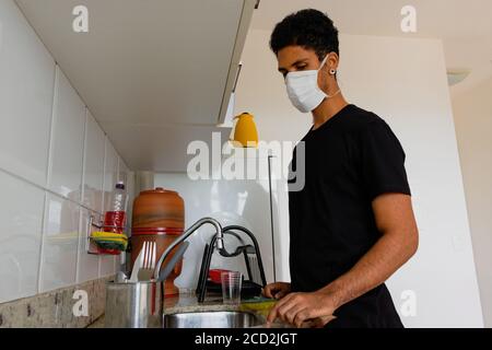 Mann Erwachsene schwarz trägt Coronavirus Maske waschen Dishe in der Küche. Stockfoto