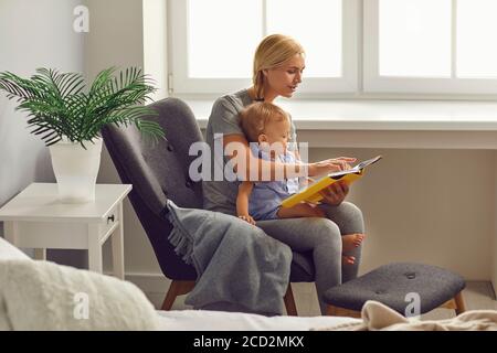 Mutter und Kind Kleinkind liest eine Geschichte in einem Buch in einem Zimmer mit Fenster. Muttertag. Stockfoto