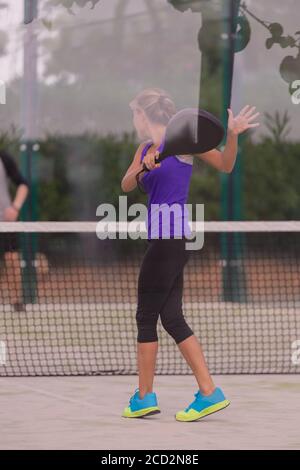 Frau hält einen Paddelschläger, nachdem sie einen Schuss auf einen Paddle Court auf einem unscharf Hintergrund zurückgegeben hat. Paddel- und Lifestyle-Konzept. Stockfoto