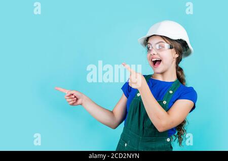 Schauen Sie hier. Kleines Mädchen in Hut spielen in der Werkstatt. Kinderschutz und Sicherheit. Kleine lächelnde Baumeister im Helm. Glückliche Kindheit. Karriere Anleitung Idee. Portrait von kleinen Mädchen mit Hut. Stockfoto