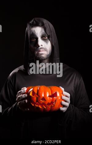 Gruseliger Grusel hält einen Kürbis über schwarzem Hintergrund, Halloween-Outfit. Stockfoto