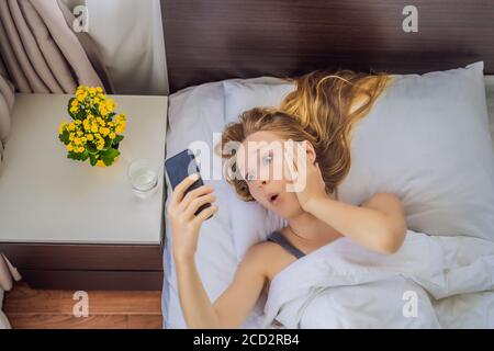 Verschlafen Frau mit überraschter Ausdruck beim Blick auf Telefon nach Ich habe den Wecker verpasst und bin spät aufgewacht Stockfoto