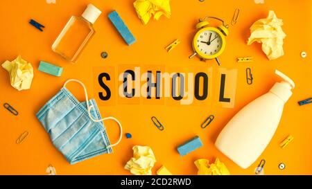 Text SCHULE auf gelbem Hintergrund mit Schulbedarf, Schutzmaske und Desinfektionsmittel antiseptisch. Zurück zur Schule. Neuer Normalwert. Schulquarantäne Stockfoto