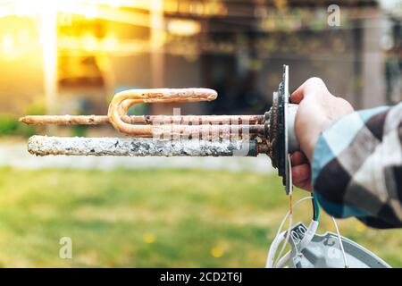 Die Hand eines weißen Mannes, zeigt die zerstörerische Wirkung der Skala auf das Element des Kessels. Stockfoto
