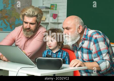 Vatertag. Ältere ältere Vater und Sohn mit Laptop, während in einem Klassenzimmer mit Kind Schüler während einer Lektion in modernen Smart School sitzen. Bildung Stockfoto