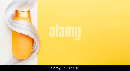 Shampoo-Flasche in Sperre von blonden Haaren auf orangefarbenem Hintergrund gewickelt. Gold Flasche Shampoo in gefärbten Haar Strang. Kopiespeicherplatz in der Draufsicht. Haarpflege Stockfoto