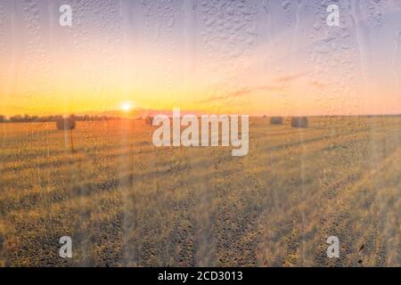 Ein landwirtschaftliches Feld mit Heuhaufen, beleuchtet von Abendsonne nach Regen, hinter nassem Glas im Herbst. Das Konzept der Änderung von schlechtem Wetter zu g Stockfoto