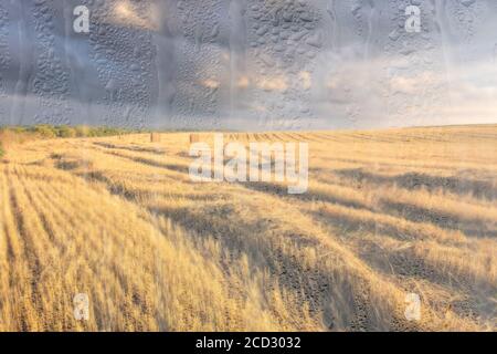 Ein landwirtschaftliches Feld mit Heuhaufen, beleuchtet von Abendsonne nach Regen, hinter nassem Glas im Herbst. Das Konzept der Änderung von schlechtem Wetter zu g Stockfoto