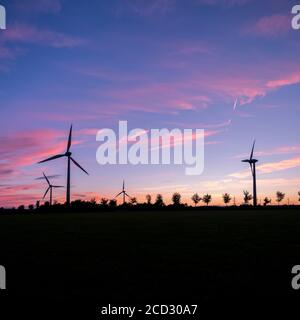 Windturbinen und Bäume bilden Silhouetten gegen den bunten Sonnenuntergang Stockfoto