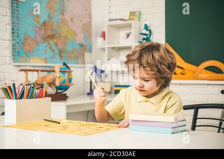 Nette Schüler mit lustigen Gesicht Schularbeit. Kinder machen sich bereit für die Schule. Freundliches Kind im Klassenzimmer in der Nähe der Tafel. Stockfoto