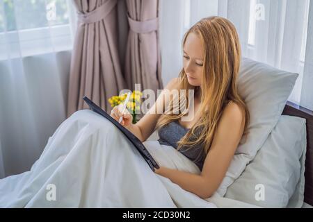 Frau zeichnet auf Tablet mit Stift im Bett Stockfoto