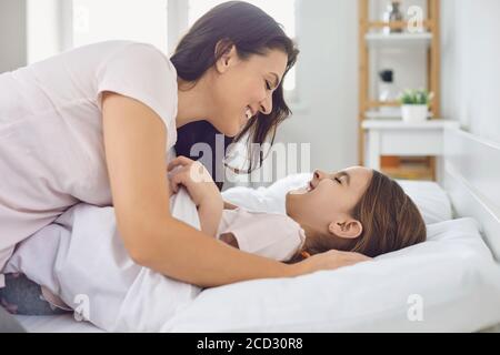 Familienbindung. Glückliche Mutter umarmt ihre Tochter auf dem Bett zu Hause. Eltern und Kinder kuscheln sich im Schlafzimmer zusammen Stockfoto