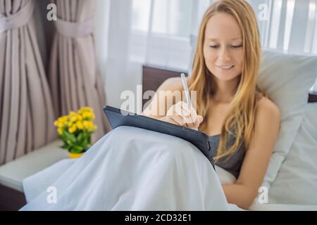 Frau zeichnet auf Tablet mit Stift im Bett Stockfoto