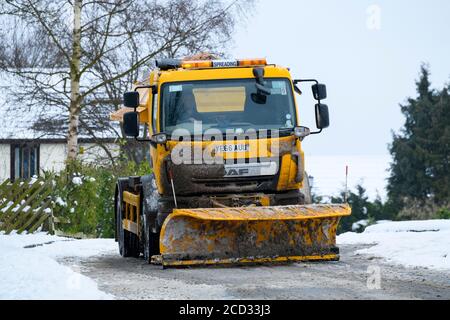 Kalt verschneiten Wintertag (rat Streuwagen, Schneepflug, Mann arbeiten & fahren, Splitt, Clearing Straße) - Menston, West Yorkshire, England Großbritannien Stockfoto