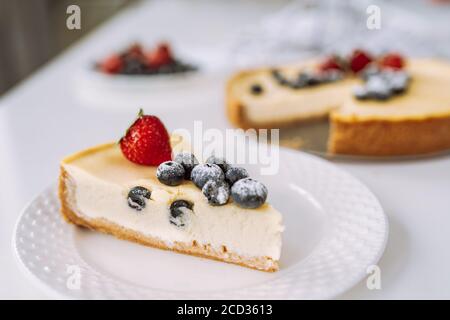 Stück hausgemachter Käsekuchen mit frischer Erdbeere und Brombeere auf einem weißen Teller auf einem Tisch. Stockfoto