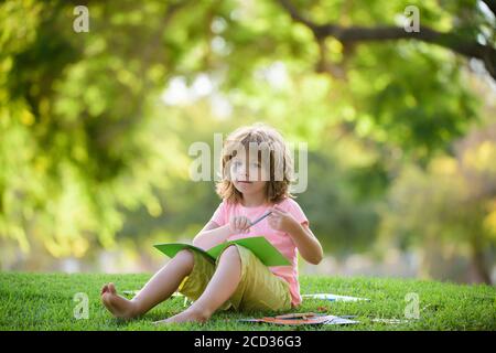 Kindererziehung im Freien. Ein kleiner Junge Schülerin genießt ihr Lernen im Park. Stockfoto